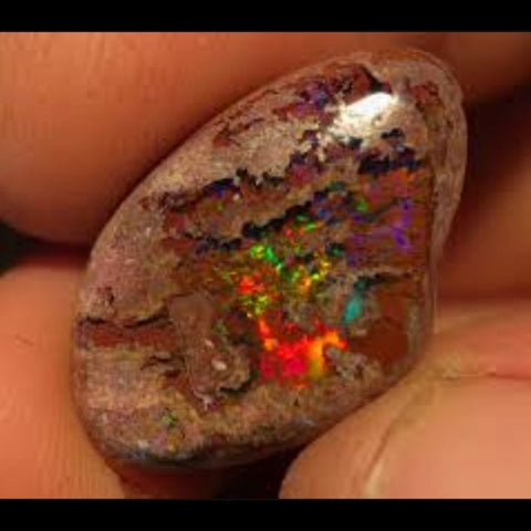 Close up of small rock held in fingers with a clear pool of opal with rainbow flashes