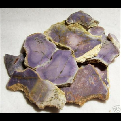 Pile of purple burro creek agate slabs on white background