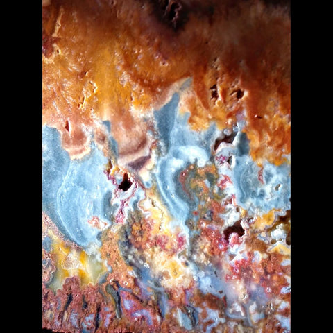 Colorful plume agate jasper cryptocrystalline rock with patterns rEaching for the top of the image with blue and orange colors