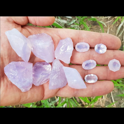 Light skinned hand holding purple pink translucent rough and faceted pieces of Lavender Moon Quartz