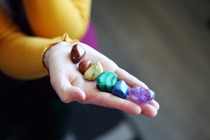 Hand holding six stones one each color of the rainbow
