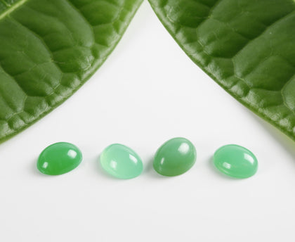 Four green stone cabochons next to two leaves