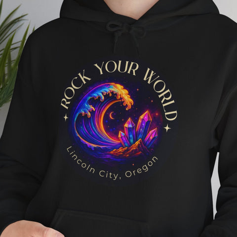 Person wearing a black hoodie with a colorful design and text, standing indoors next to a plant.