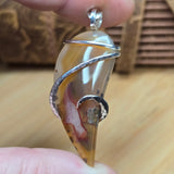 Close-up of a silver pendant with a natural stone held between fingers on a wooden surface.