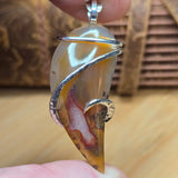 Close-up of a silver and agate pendant held between fingers on a wooden surface.