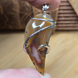 Close-up of a silver and amber agate pendant held between fingers on a wooden surface.