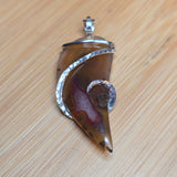 Brown agate pendant with silver setting on a wooden surface
