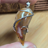 Hand holding a pendant with an agate and silver wire wrapping on a wooden surface.