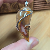 Close-up of a hand holding a silver agate pendant with a tortoiseshell band against a wooden background