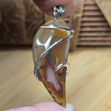 Hand holding a pendant with a clear stone and silver wire wrap against a blurred background