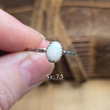 Silver ring with a white stone held by a hand against a blurred background