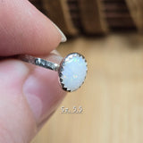 Close-up of a silver ring with a white gemstone held between fingers on a blurred background