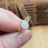Silver ring with a white gemstone held between fingers against a wooden background