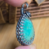 Green pendant with silver filigree on a wooden surface