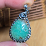 Chrysoprase pendant with silver frame held between fingers on a wooden surface