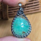 Chrysoprase pendant with silver frame held between fingers on a wooden surface