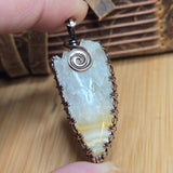 Crystal pendant with copper wire wrapping held by a hand on a wooden surface