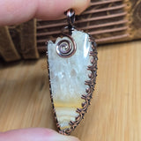 Decorative pendant with intricate design held by a hand on a wooden surface