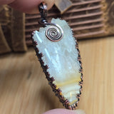 Pendant with stone and spiral design held by a hand on a wooden surface