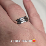 3 simple, sleek sterling silver band rings with a hammered finish, displayed on a person's hand.