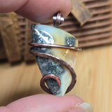 Close-up of a hand holding a unique necklace with a shell and metal wire design.