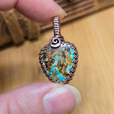Turquoise stone pendant held between two fingers with a wooden background