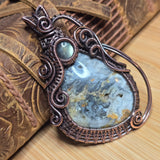 Decorative pendant with intricate copper wirework on a textured surface