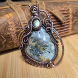 Wire wrap Pendant with blue stone and intricate copper design on a wood and leather surface