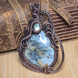 Decorative pendant with blue stone and intricate copper wirework on a textured surface