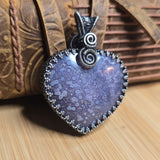 Heart-shaped pendant with textured surface and silver detailing on a wooden background
