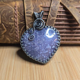 Purple heart-shaped pendant with silver detailing on a wooden surface