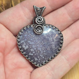 Purple patterned pendant with silver wire wrapping held in a hand
