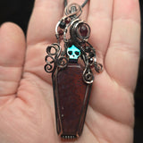 Red moss agate coffin pendant with antiqued copper wirework, garnet accents and an iridescent green skull.