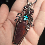 Red moss agate coffin pendant with antiqued copper wirework, garnet accents and an iridescent green skull.