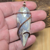 Hand holding a stone pendant with copper wire wrapping