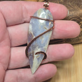 Hand holding a stone pendant with copper wire wrapping on a wooden surface