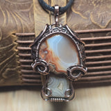 Copper mushroom agate pendant with a decorative stone on a textured wooden background
