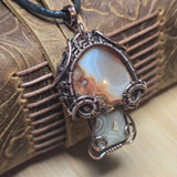 Copper wrapped pendant with a natural stone on a textured surface