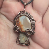 Close-up of a decorative pendant with intricate wirework held in a hand.