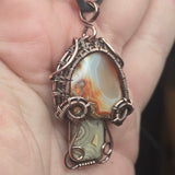 Close-up of a copper-wrapped pendant with agate stone on a hand.