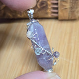 Purple crystal pendant with silver wire wrapping held between fingers on a wooden surface