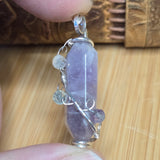 Amethyst crystal pendant with silver wire wrapping held by a hand on a wooden surface
