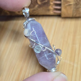 Purple crystal pendant with silver wire wrapping held by a hand on a wooden surface