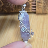 Crystal pendant with silver wire wrapping held between fingers on a wooden surface