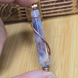 Hand holding a purple crystal pendant with copper accents on a wooden surface
