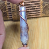 Crystal pendant with copper wire wrapping held by a hand on a wooden surface