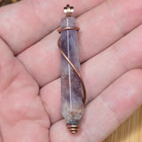 Amethyst crystal pendant with copper wire wrapping held in a hand.