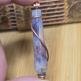 Purple crystal pendant with copper wire wrapping held by a hand on a wooden surface