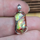 Ammolite pendant with silver wire wrapping held between fingers