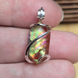 Ammolite pendant with silver wire wrapping held between fingers